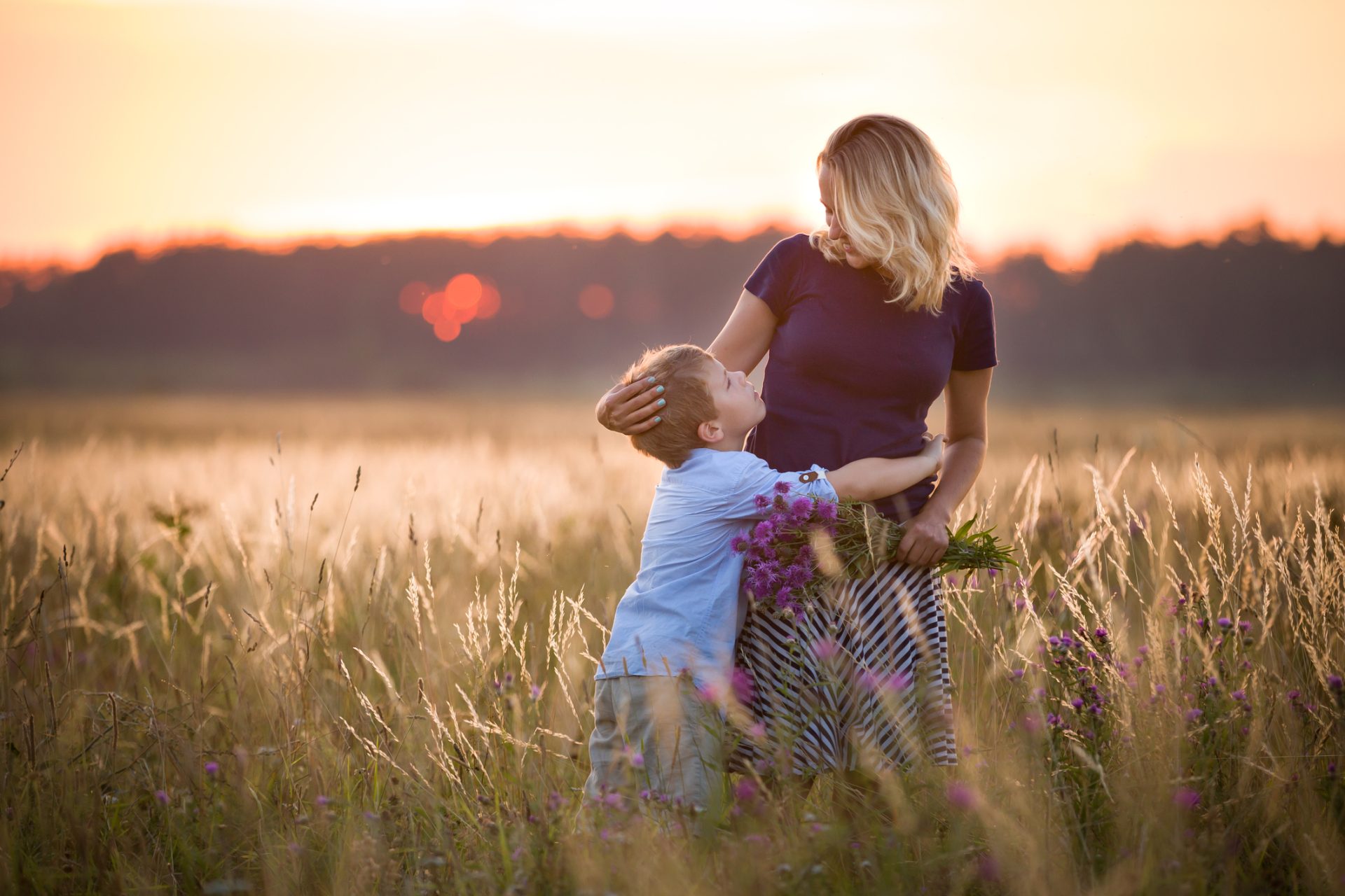Cute kid boy hugging his mother on a summer meadow
