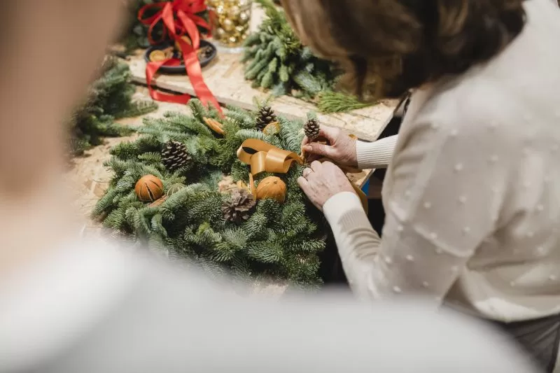 Close up shot of a woman adding pine cone decorations to her homemade christmas wreath